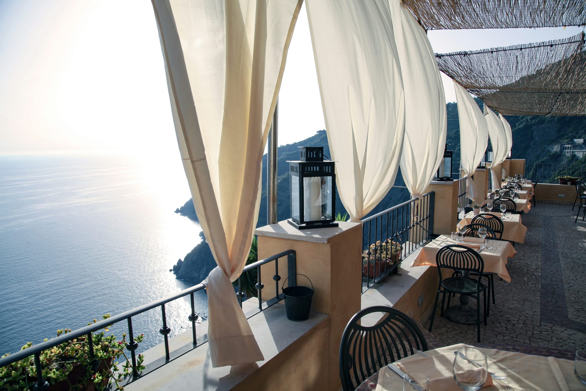 Eine ruhige Terrasse mit wehenden weißen Vorhängen und Blick auf das Meer im Abendlicht